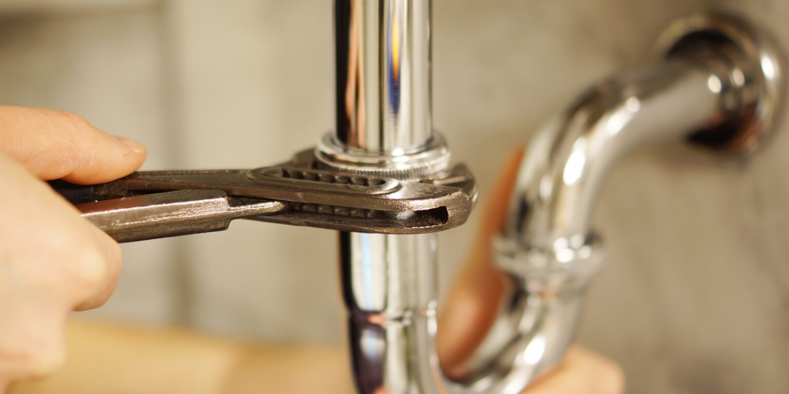 Plumbing repair service. Professional installer with spanner checking pipe.